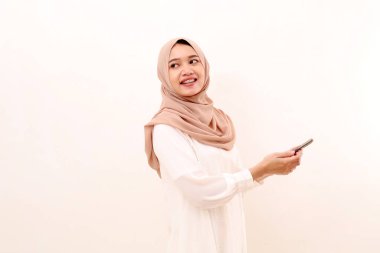 Happy young asian muslim woman looking back while holding a cell phone. Isolated on white background