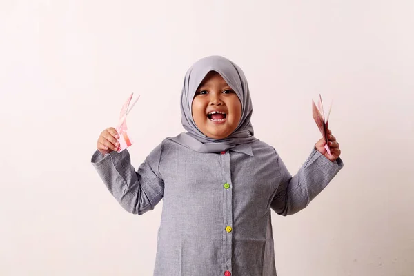 インドネシアの紙幣を持ちながら立つ興奮したアジア系ムスリムの少女 アイド フィトルのコンセプト — ストック写真
