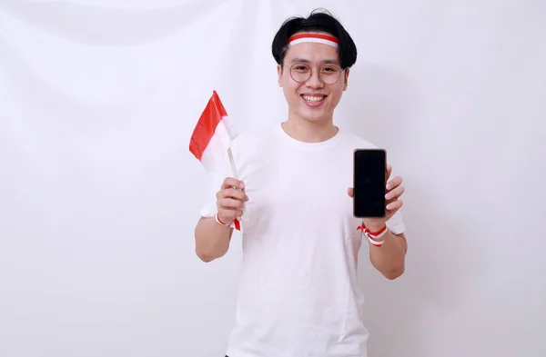 亚洲男子举旗庆祝印度尼西亚独立日 并展示空白手机屏幕 — 图库照片