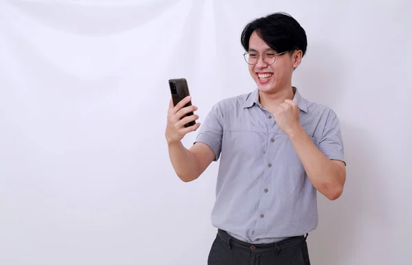 携帯電話を持ちながら立っている幸せな興奮したアジア人男性 白に隔離された — ストック写真