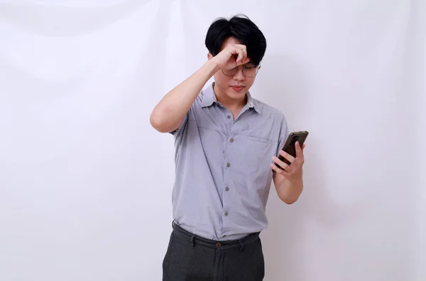 頭を抱えながら携帯電話を持っているアジア系男性のストレス 白に隔離された — ストック写真