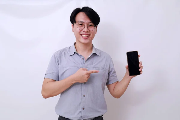 幸せなアジアの男は彼の空白の携帯電話のディスプレイを指す 白に隔離された — ストック写真
