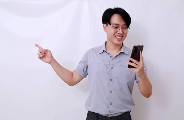 Happy Asian Man Holding Cell Phone While Pointing Sideways Isolated — Stock Photo, Image