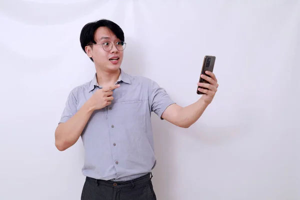 携帯電話を持っているアジア人の男がそれを指してショックを受けました 白に隔離された — ストック写真