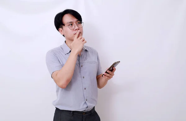 Förvirrad Asiatisk Man Som Håller Mobiltelefon Medan Han Tänker Något — Stockfoto