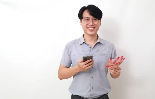 Glad Asiatisk Man Med Indonesiska Sedlar Och Mobiltelefon Isolerad Vitt — Stockfoto