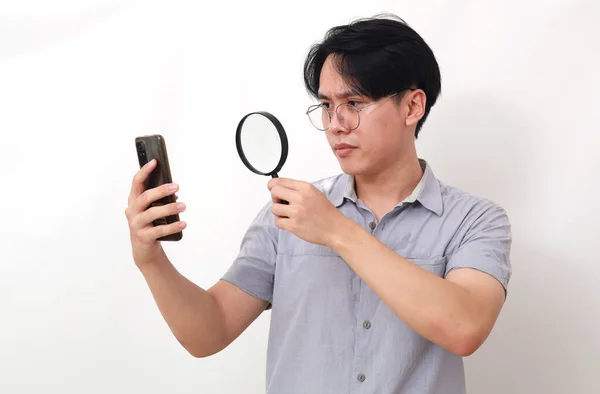 Nyfiken Asiatisk Man Tittar Sin Mobil Genom Förstoringsglas Isolerad Vitt — Stockfoto