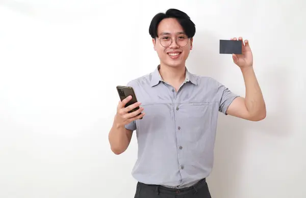 快乐的亚洲男人拿着手机 拿着空白卡片 因白人背景而被隔离 — 图库照片