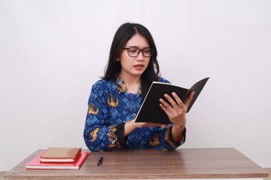 Batik Korpri giymiş kafası karışmış bir Asyalı kadın, Endonezya 'nın geleneksel işçi üniforması kitap okuyor.