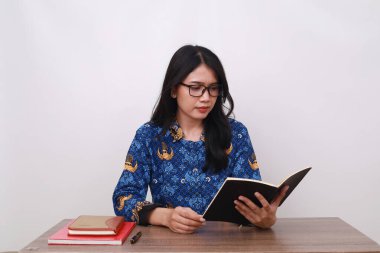 Batik Korpri giymiş güzel bir Asyalı kadın, Endonezya 'nın geleneksel işçi üniforması kitap okuyor.