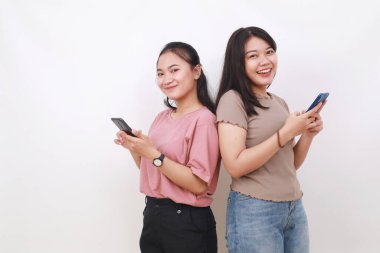 İki Asyalı kadın el ele tutuşup cep telefonlarıyla internette sohbet ediyorlar.