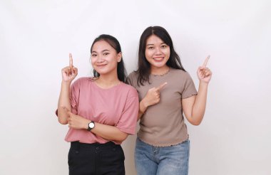 İki Asyalı kadın kameraya bakarken iki tarafı işaret ediyor. Beyaz arkaplanda izole