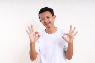 Asyalı komik adam el hareketi yaparken ayakta duruyor. Beyaz arkaplanda izole