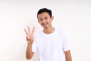 Asyalı komik adam üç parmağını gösterirken ayakta duruyor. Beyaz arkaplanda izole