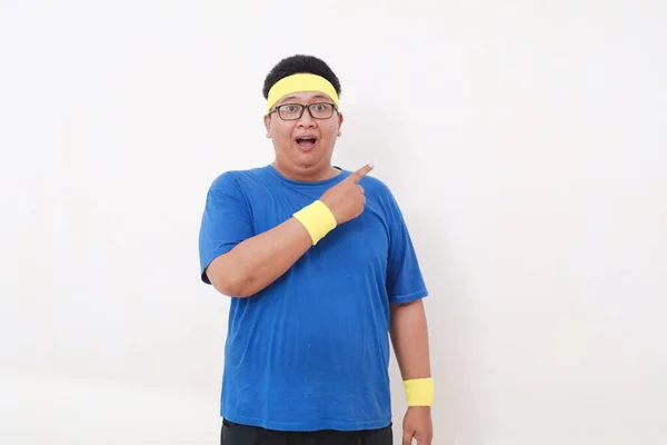 アジアの太りすぎの男のすごい顔の表現でスポーツウェアポインティング横に空白のスペース — ストック写真