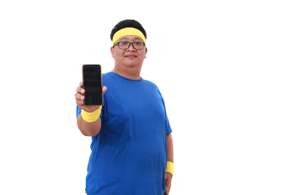 快乐的亚洲超重男子穿着运动服站在那里 展示着空白的手机显示屏 被隔离了 — 图库照片
