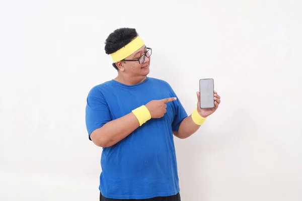 快乐的亚洲超重男子穿着运动服站在那里 展示着空白的手机显示屏 被隔离了 — 图库照片