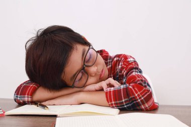 Yorgun Asyalı öğrencinin çalışırken masada uyuduğu fotoğrafı kapat. Beyazda izole edilmiş