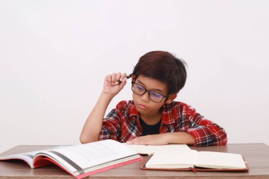 Asyalı öğrenci ciddi ciddi masada çalışıyor. Beyaz arkaplanda izole