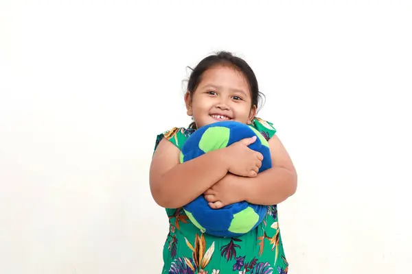 Szczęśliwy Azjata Dzieciak Stojący Podczas Przytulania Jej Zabawki Piłkę Odizolowane — Zdjęcie stockowe