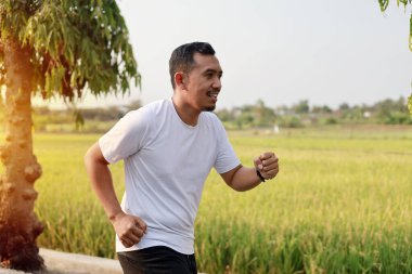 Asyalı adam dışarıda koşuyor, doğada çalışıyor.