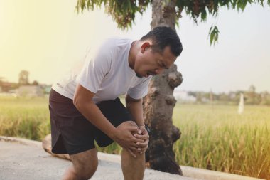 Açık havada egzersiz yaparken diz ağrısı çeken Asyalı bir adam.