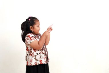 Batik 'li sevimli Asyalı küçük kız yanlamasına işaret etti. Beyaz arkaplanda izole