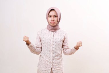 Kızgın, mutsuz, Asyalı, genç, Müslüman kadın yumruklarıyla kameraya bakıyor. Beyazda izole edilmiş