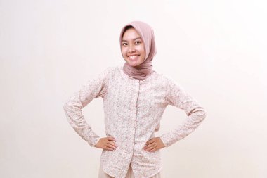 Neşeli Asyalı genç Müslüman kadın kameraya bakarken ayakta duruyor. Beyazda izole edilmiş