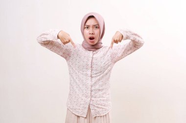 Mutsuz genç Asyalı Müslüman kadın parmaklarıyla işaret ederken ayakta duruyor. Beyazda izole edilmiş