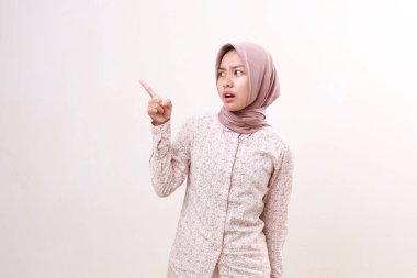 Kafası karışmış genç Asyalı Müslüman kız boş uzayda onu işaret ederken ayakta duruyor. Beyazda izole edilmiş
