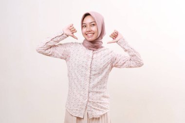 Kendine güvenen genç Asyalı Müslüman kadın kendini işaret ederek ayakta duruyor. Beyazda izole edilmiş