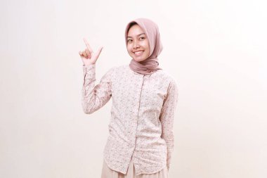 Yukarıyı göstererek ayakta duran mutlu Asyalı genç Müslüman kadın. Beyazda izole edilmiş