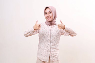 Asyalı genç müslüman kadın başparmağını kaldırarak ayakta duruyor. Beyaz arkaplanda izole
