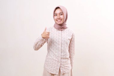 Asyalı tatmin olmuş genç Müslüman kadın başparmağıyla kabul işareti gösterirken ayakta duruyor. Beyazda izole edilmiş