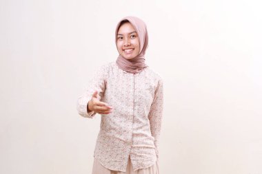 Genç, dost canlısı Asyalı Müslüman kadın elini uzatırken ayakta duruyor. Beyaz arkaplanda izole