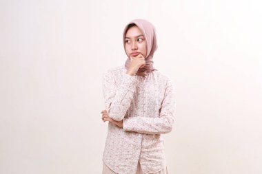 Düşünceli genç Asyalı müslüman kadın hayal kurarken ve yan bakarken ayakta duruyor. Beyazda izole edilmiş