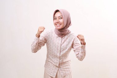 Heyecanlı Asyalı genç Müslüman kadın başarısını yumruklarıyla kutluyor. Beyazda izole edilmiş