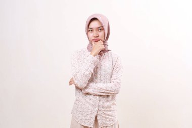 Düşünceli genç Asyalı Müslüman kadın kameraya bakıp düşünürken ayakta duruyor. Beyaz arkaplanda izole