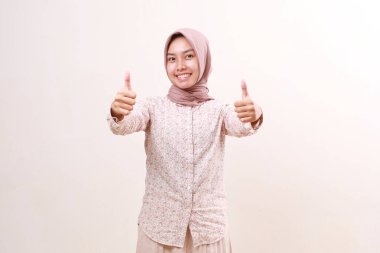 Mutlu Asyalı genç Müslüman kadın başparmağını kaldırırken ayakta duruyor. Beyaz arkaplanda izole