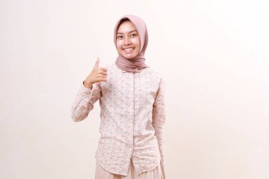 Mutlu Asyalı genç Müslüman kız başparmağını kaldırırken ayakta duruyor. Beyaz arkaplanda izole