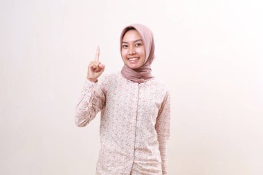 Parmağını gösterirken ayakta duran mutlu Asyalı genç Müslüman kız. Beyaz arkaplanda izole