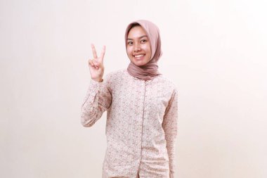 İki parmağını göstererek ayakta duran mutlu Asyalı genç Müslüman kız. Beyaz arkaplanda izole
