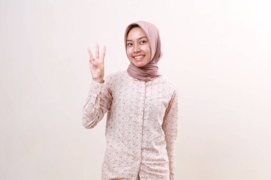 Üç parmağını göstererek ayakta duran mutlu Asyalı genç Müslüman kız. Beyaz arkaplanda izole