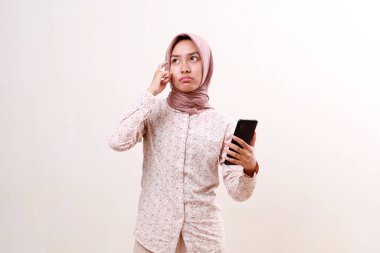 Düşünceli Asyalı genç Müslüman kız bir şey düşünürken elinde cep telefonu tutuyor. Beyazda izole edilmiş