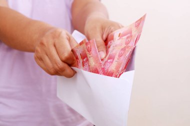 Beyaz zemin üzerinde Endonezya banknotları olan bir zarf tutan eller. Kadın eli bir zarftan para çekiyor, yakın plan. Rüşvet, maaş, kazanç ve tasarruf kavramı