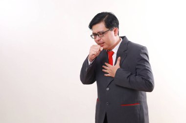 Asyalı işadamı öksürürken beyaz duvara yaslanmış.