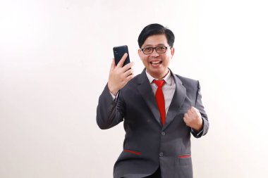 Vay be, Asyalı iş adamı cep telefonu ve yumruğunu tutarak başarıyı kutluyor.