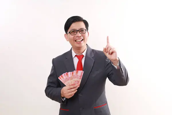 Excited asian businessman holding Indonesia banknotes while pointing above. Isolated on white