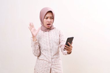 Shocked young asian muslim girl standing while getting message from her cell phone. Isolated on white